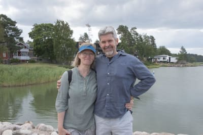 En man och en kvinna står framför vattnet och tittar in i kameran.
