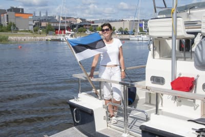 Kvinna står på en båt, Estlands flagga vajar framför henne.