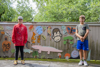 På bilden står två unga pojkar och poserar vid en vägg var de har målat konst.