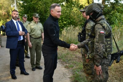 Polens president, klädd i helsvart, skakar hand med två soldater i camouflageuniformer.