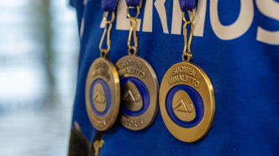 Närbild på tre medaljer med texten Suomen uimaliitto, Finlands simförbund.
