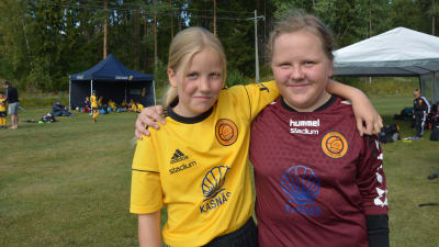 Tindra Eggert i gul fotbollskjorta och Julia Hakkarainen i lila målvaktströja, håller armarna om varandra.