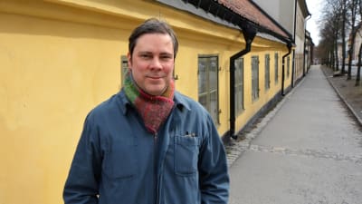 Jukka Rintamäki står i stadsmiljö framför en gul låg husfasad.