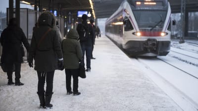 Tåg anländer till perrong, människor står och väntar