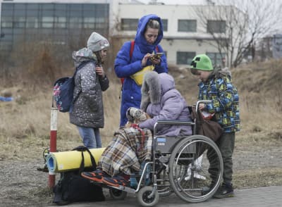 En flicka, en kvinna och en pojke står bakom en gammal kvinna i rullstol.