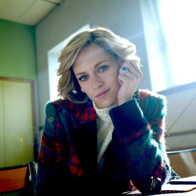 På bilden ses skådespelaren Kristen Stewart i rollen som prinsessan Diana. Hon sitter iklädd en röd och grön blazer. Hon sitter i ett rum med motljus med vänstra armen lutad mot ett bord och handen håller hon mot sin vänstra kind.