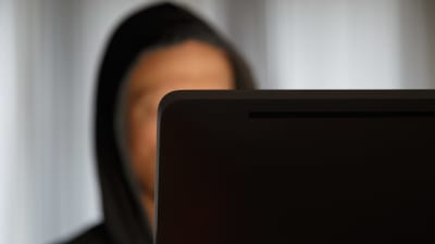 ung man vars ansikte inte syns sitter framför en bärbar dator