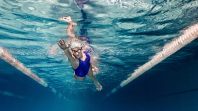 En kvinna simmar i en simbassäng. Bilden är tagen under vattnet.