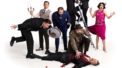 Sju skådespelare står kring en liggande kropp i humoristiska poser mot en vit bakgrund.