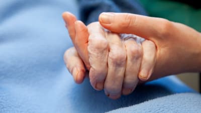 En yngre person håller en äldre person i handen.