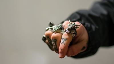 En hand som visar knogarna, tatuerade fingrar och ringar.