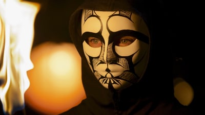 En flicka med en svart luvtröja har en svartvit mask över ansiktet och håller i en brinnande fackla.