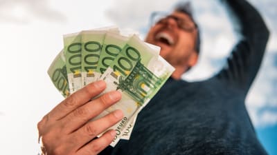 En man håller en knippe 100-eurossedlar handen och skrattar och jublar.