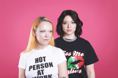 Radiojuontajat ja dj:t Taika Mannila ja Lina Schiffer poseeraavat pinkkiä taustaa vasten.