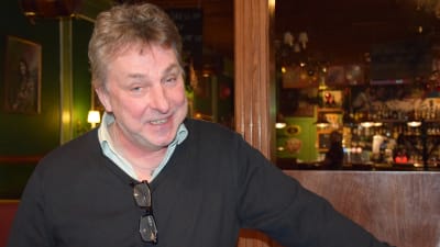 En man i en pu . Han ler och har huvudet lite på sned.