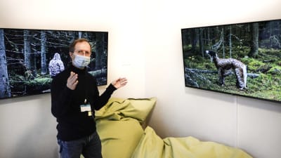 Man med munskydd visar två skärmar i ett rum. På skärmarna bilder från skog.