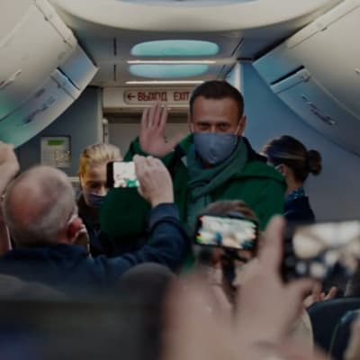Alexei Navalny vinkar till journalister ombord på ett flygplan.