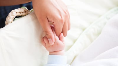 Kvinnohand håller i en babyhand vid en babysäng.