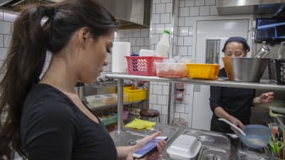 Ninni Nguyen ser på sin smarttelefon medan hon står i köket i föräldrarnas vietnamesiska restaurang.