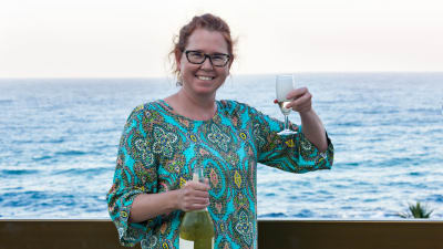 Glad kvinna skålar med vin på en strand. 