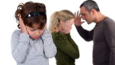Barn sätter händer mot öronen medan föräldrarna grälar. 