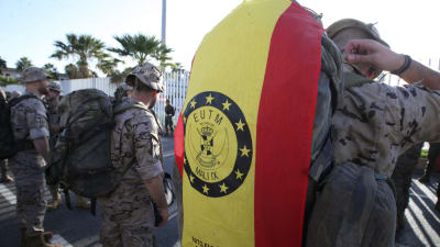 Soldater står med sina ryggsäckar vid en avskedesceremoni i Ceuta den 5 november 2016 inför deras avresa till EU:s krishanteringsoperation i Mali. I närbild en flagga med förkortningen EUTM (European Union Training Mission in Mali). 