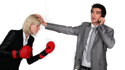 en kvinnlig kollega med boxningshandskar står mot en manlig kollega som ignorerar kvinnan, talar istället i telefonen.