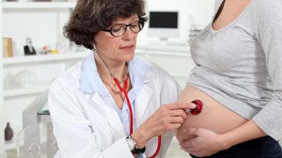 läkare lyssnar med stetoskop på en gravid mage