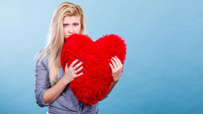 Sorgsen blond kvinna med röd hjärtformad kudde i famnen