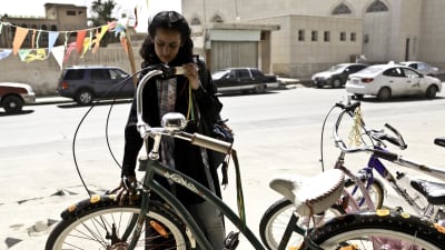 Wadjda (Waad Mohammed) står bredvid en grön cykel och ser drömmande på den.
