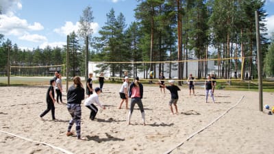 Ungdomar spelar beachvolleyboll på en sandig plan vid en idrottsanläggning.