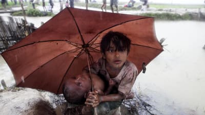 En rohingyaflicka skyddar sin lillasyster med paraply från regnet