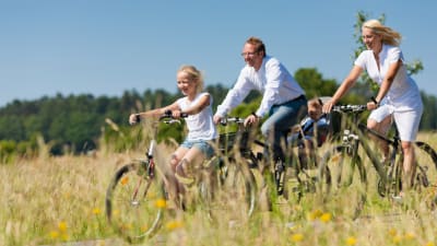 en medelålders man och en medelålders kvinna är ute på cykeltur med sin dotter en sommardag.