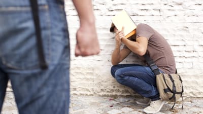 en man sitter tryckt mot en vägg, en annan står med knuten näve och tittar