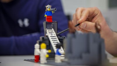 En legokung med megafon på en piedestal med stege, andra gubbar nedanför. 