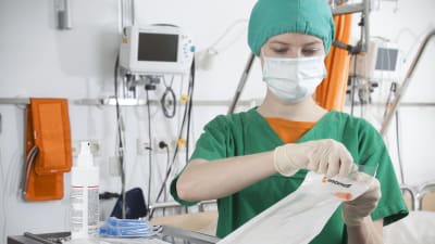 Skötare med ansiktsmask öppnar engångsförpackning med vårdartikel.