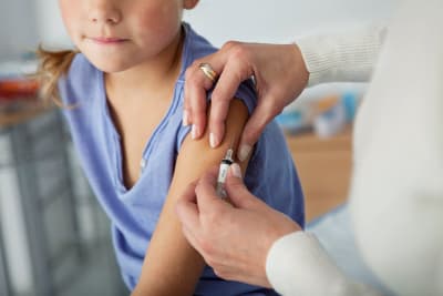 En flicka vaccineras med en spruta i armen.