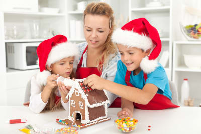 mamma och två barn dekorerar ett pepparkakshus