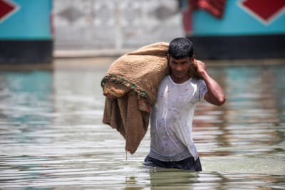 Ung man vadar i flodvattnet i Bangladesh under översvämningarna 2022.