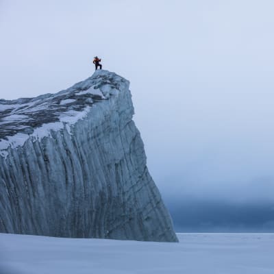 En person står uppe på en glaciärkant i Antarktis. 