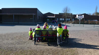Barn samlade kring lärare som läser utomhus.
