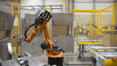 En orange robot som monterar ihop paket i postens logistikcentral för näthandel i Vanda.