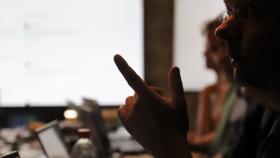 Bild av en person i profil tagen i motljus mot en ljus skärm. Personen håller upp et finger och talar uppenbarligen. 