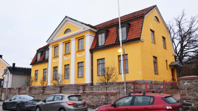 På bilden syns ett stort gult hus med vita detaljer.
