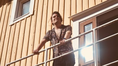 Musikern André Linman utomhus på en trappavsats, tittar upp mot solen.