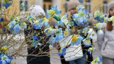 Elever säljer kvistar ned gulblå blommor på ett torg.