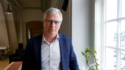 Man med blå kavaj och glasögon står vid ett fönster.