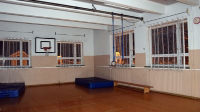 En liten gymnastiksal med basketställning och blåa madrasser.
