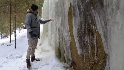 Wilhlem står vid ett isfall i skogen. Han håller handen under en istapp och vattnet droppar.