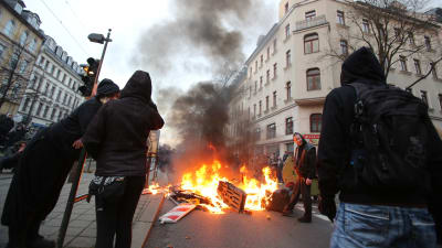 Vänsteranhängare står vid en brinnande barrikad efter våldsam motprotest mot nynazistisk demonstration.